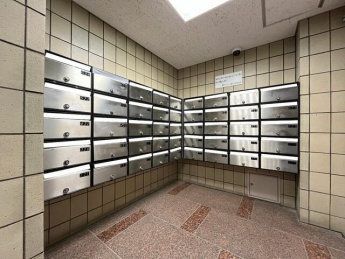 【共用部】整然と並ぶ集合郵便受け。上部には防犯カメラが設置さ